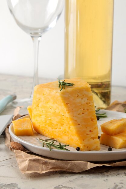 Slices of delicious marble cheese with a sprig of rosemary, honey and a cheese knife and white wine on a plate on a light concrete background.