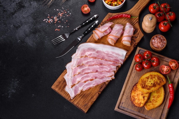 Slices of delicious raw or salted bacon with spices salt vegetables and herbs on a wooden cutting board