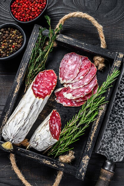 Slices of dry cured salchichon salami in a wooden tray. Black wooden background. Top view.