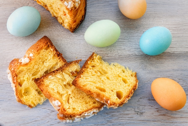 Slices of Easter cake and colorful eggs are on a wooden table top.