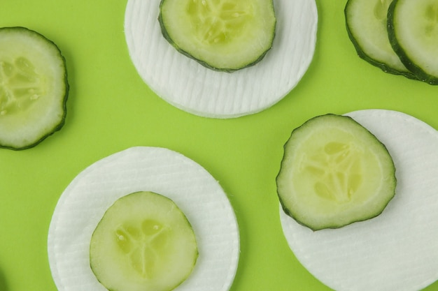 Photo slices of fresh cucumber and cotton sponge on a bright green background. cucumber cosmetics concept. skin care. tonic cucumber extract