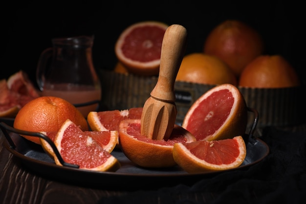 Slices of fresh grapefruit prepared for making fresh squeezed juice on a platter, dark background