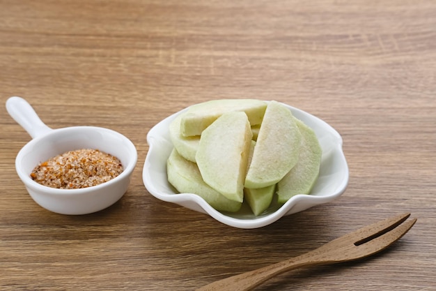 Slices of fresh guava fruit with a sprinkling of chili and salt served in white plate