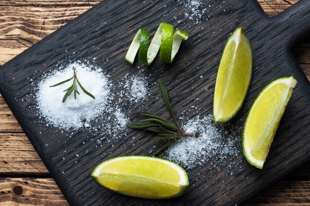 Foto fette di lime fresco, sale e rosmarino su un tagliere di legno.