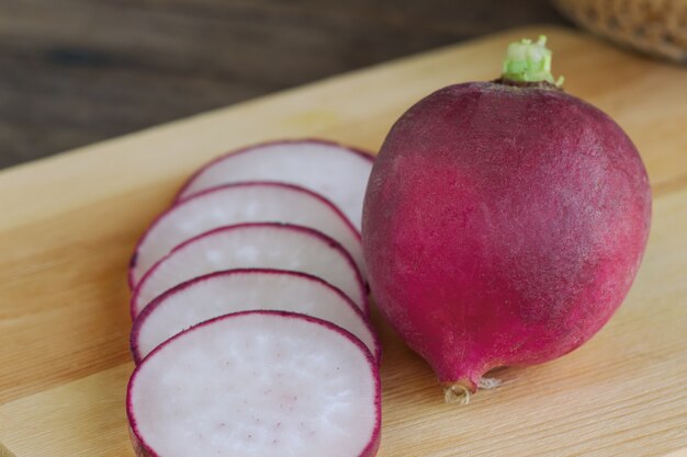 Slices fresh red radish by kitchen knife and wood cutting board on wooden table.