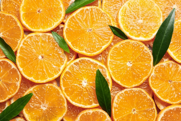 Slices of fresh ripe tangerines and leaves as background top view citrus fruit