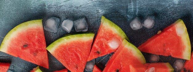 Slices of fresh watermelon with ice on a blue concrete background. Detox and vegetarian concept. Top view, copy space, banner.