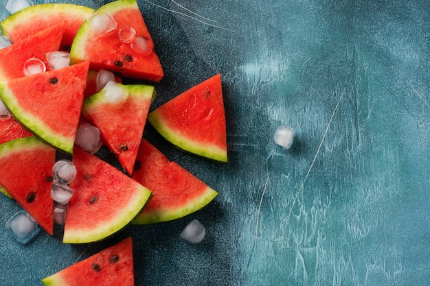 Slices of fresh watermelon with ice on a blue concrete background. Detox and vegetarian concept. Top view, copy space, banner