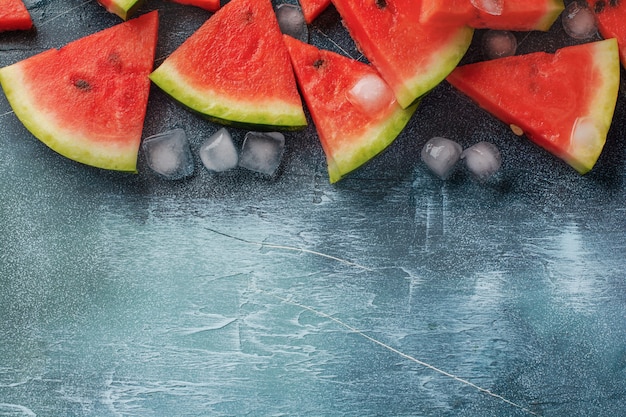 Foto fette di anguria fresca con ghiaccio su uno sfondo di cemento blu. detox e concetto vegetariano. vista dall'alto, copia spazio, banner