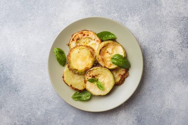 Slices of fried zucchini in batter with garlic and Basil on a plate.