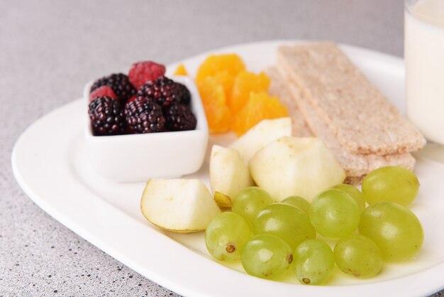 Ломтики фруктов с хрустящими хлебцами и стаканом молока на тарелке на столе крупным планом