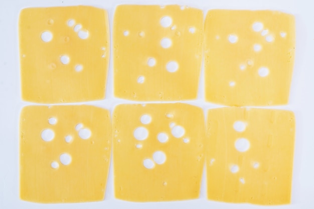 Slices of hard cheese with holes on white as a background.