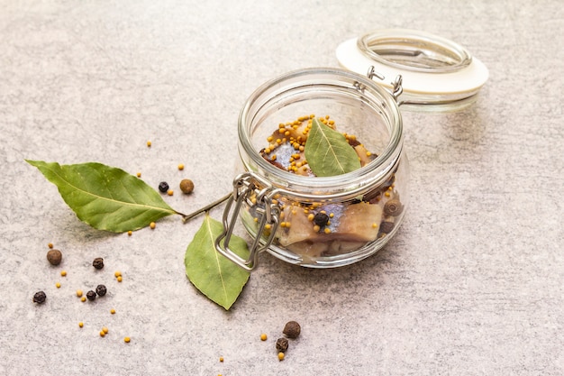 Slices of herring with spices in a glass jar.