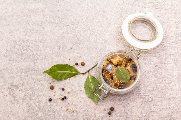 Slices of herring with spices in a glass jar.