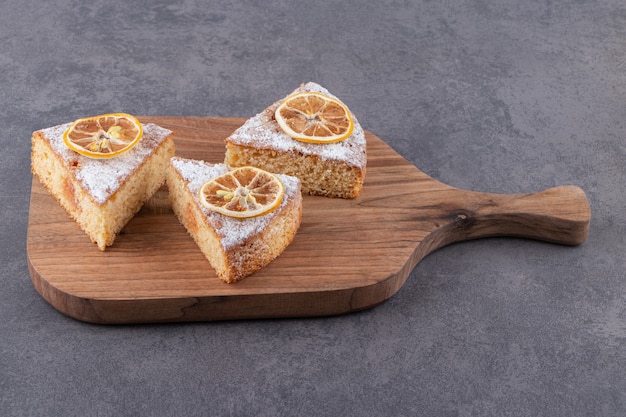 Slices of homemade cake with lemons placed on wooden board.