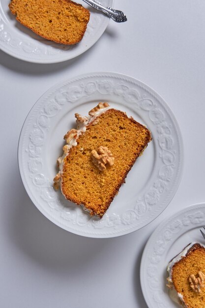 Slices of homemade carrot cake with sugar glaze and walnuts served in three white dishes. Vegan food