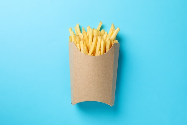 Slices of hot french fries in box on blue. Top view