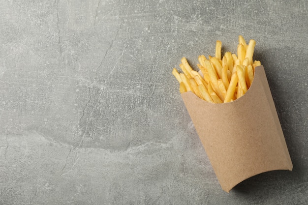 Slices of hot french fries in box on grey. Top view