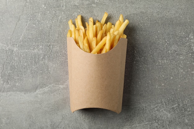 Slices of hot french fries in box on grey. Top view