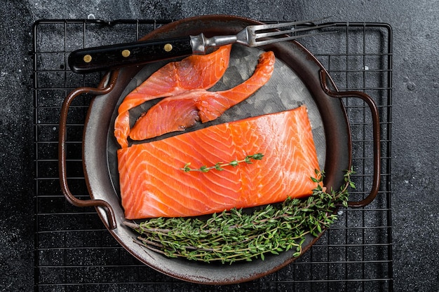 Slices of lightly salted salmon with thyme in a steel tray Black background Top view