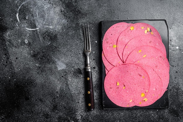 Slices of meat salami sausage with pistachios nuts on marble board Black background Top view Copy space