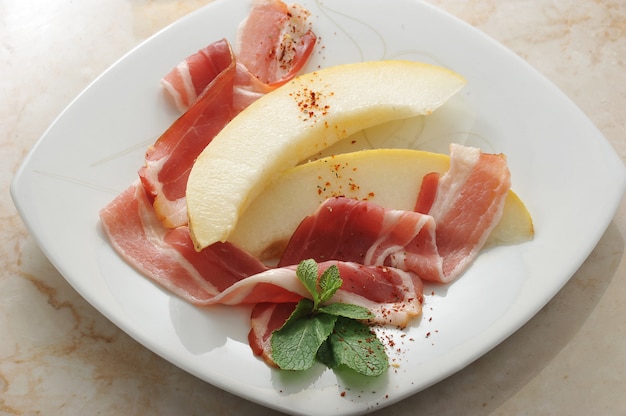 Slices of melon wrapped in bacon with mint leaves on marble