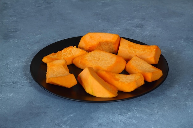 写真 黒い背景にステンレス製のボウルにオレンジ黄色の果肉を持つ生のカボチャのスライス