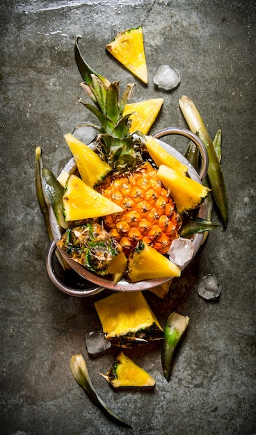 Slices of pineapple from a whole pineapple , leaves and ice in a saucepan.