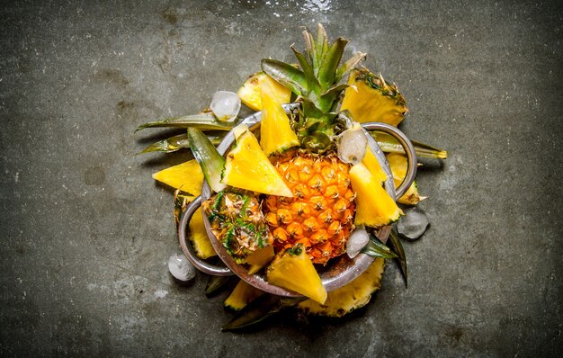 Slices of pineapple from a whole pineapple , leaves and ice in a saucepan.