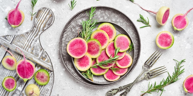 Slices of pink watermelon radish on a plate. Dietary useful vegetables. On a gray stone background.