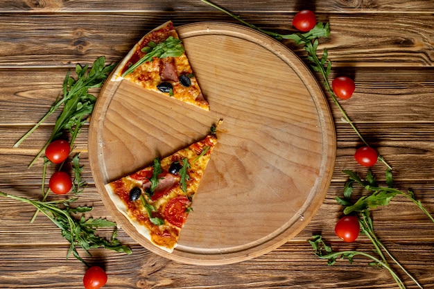 Slices Pizza on wooden board, with tomatoes and basil, Italian style on old wooden table, top view.