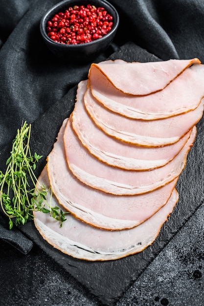 Slices of pork ham with thyme. Organic meat. Black background. Top view.