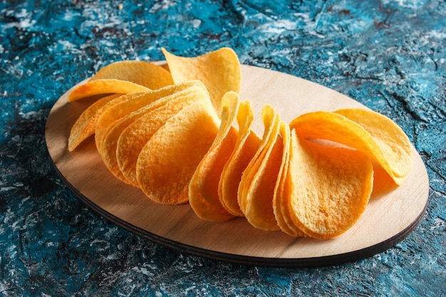 Slices of potato chips on a wooden platform on blue concrete table. Top view