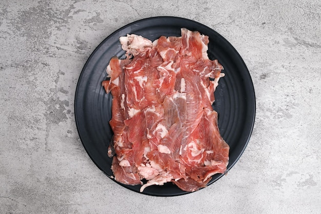 Slices of raw beef meat on a black plate over grey background