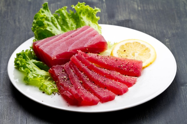 Fette di sashimi di tonno rosso crudo sul piatto bianco su backgr di legno