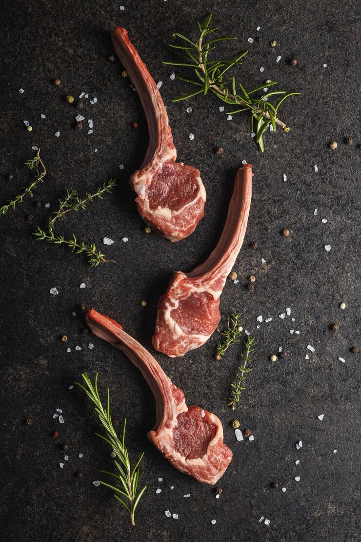 Photo slices raw lamb chops with salt pepper and rosemary on black table top view