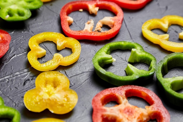 Photo slices of red green and yellow bell peppers on black background sweet peppers