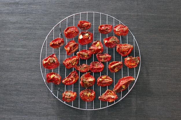 Slices of red tomatoes sun-dried arranged on round metal grid.