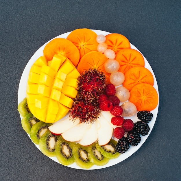 Slices of ripe exotic fruits on white plate. Kiwi, mango, raspberry, blueberry and persimmon.