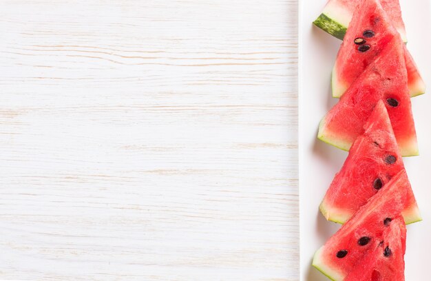 Slices of ripe fresh watermelon on the plate on white wooden table. Top view