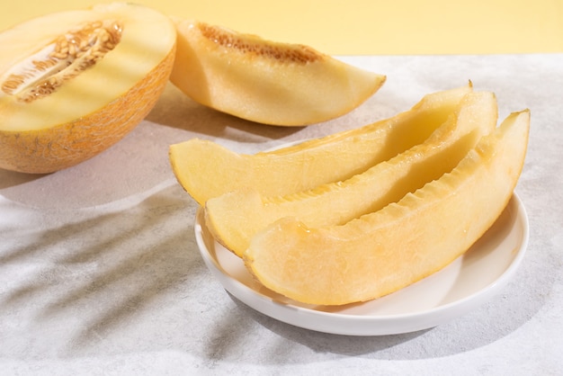 Fette di melone succoso maturo su un piatto su uno sfondo bianco e giallo con ombre, cibo sano.