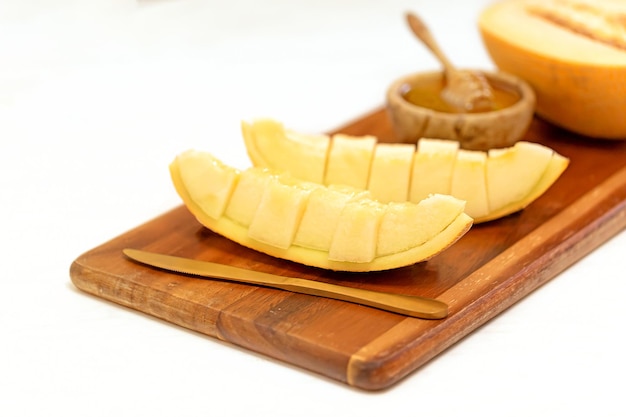 Slices of ripe melon with honey on a wooden board on a white background