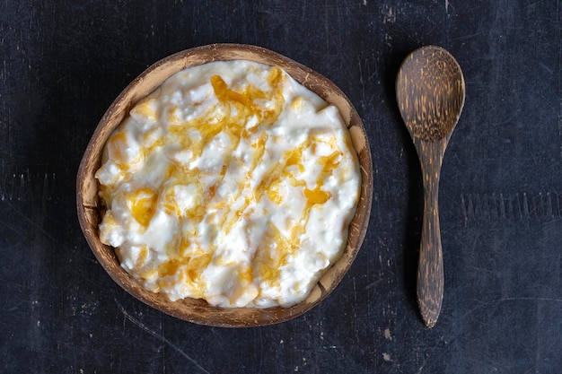 Slices of ripe sweet yellow mango fruit with white cottage cheese honey and sour cream in coconut bowl closeup