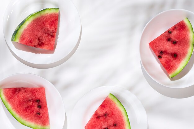 Slices of ripe watermelon on white plates on a white table. Top view, flat lay.