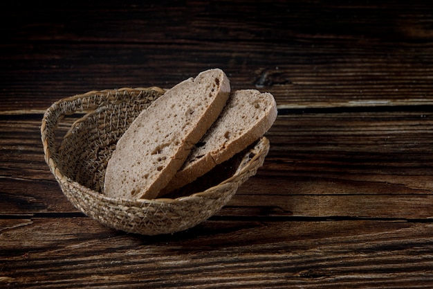 Slices of rustic bread in wicker bowl on a wood table