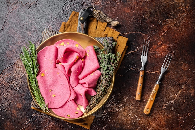 Slices of Salami with pistachios nuts in steel plate with thyme and rosemary Dark background Top view