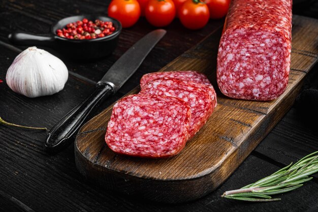 Slices of salami with vegetables set, on black wooden table background