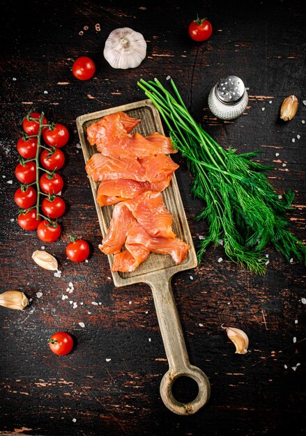 Slices of salted salmon on a cutting board with dill and tomatoes