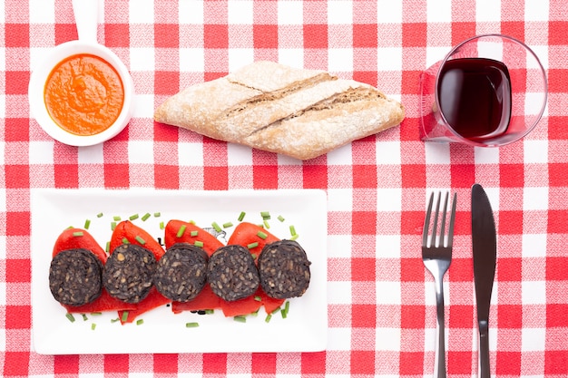 Slices of Spanish black pudding on piquillo peppers in white plate on a red checkered tablecloth