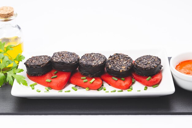 Slices of Spanish black pudding on piquillo peppers in white plate on white surface